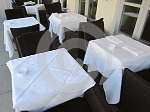 Empty tables covered in white cloths outside restaurant and cafe waiting for guests to arrive