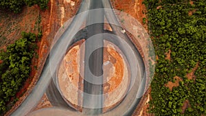 Empty tarmac road intersection circle in deep red brown landscape aerial view moving allow road green trees around