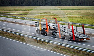 An empty tractor-trailer truck with a semi-trailer car transporter drives along the highway in the summer against the