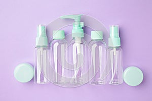 Empty travel cosmetic bottles on violet background. Minimalist bodycare beauty products for vacation or journey. Top view.
