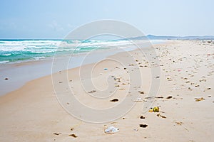 Empty tropical beach with rubbish trash plastic on sand. Waving ocean desert beach pollution problem in the sea. Sunny daytime.