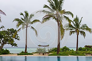 Empty tropical resort on cloudy day. Swimming pool and lounge chairs on ocean coast. Hotel resort landscape.