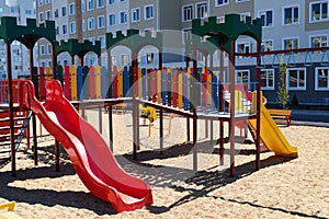 Empty urban residential infrastructure, nobody - children`s playground next to a condominium. Swing, slide, stairs, multistory