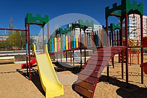 Empty urban residential infrastructure, nobody - children`s playground next to a condominium. Swing, slide, stairs, multistory