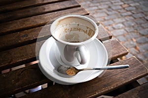 Empty, used coffee cup on wooden table in outside street cafe.