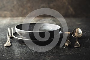 Empty vintage plate with silver knife, spoon and fork on black table