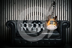 Empty vintage sofa and electric guitar with modern wood wall recording studio background. Music concept with nobody