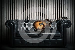 Empty vintage sofa and electric guitar with modern wood wall recording studio background. Music concept with nobody