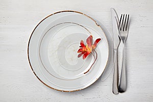 Empty vintage white ceramic plate with maple seed pods and cutlery on a white painted wooden table