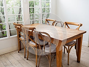 Empty vintage wood dining table set with 6 old chairs seat on wood pattern rubber tiles near glass window with tree outside.