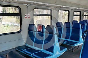 Empty wagon in train with blue chairs and red round stickers with restriction that forbid to take up middle seat in row to reduce