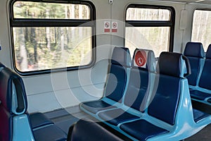 Empty wagon in train with blue chairs and red round stickers with restriction that forbid to take up middle seat in row to reduce