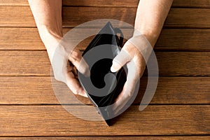 Empty wallet in the hands of an elderly man on a wooden table. T