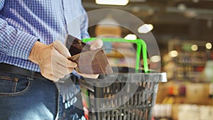 Empty wallet with no money in the hand of an older white male shopper with a shopping cart.