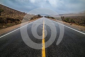 Empty wet desert asphalt pavement road with yellow highway marking lines