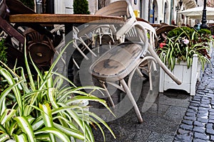 Empty wet wooden table and chairs on terrace of outdoor cafeteria during rain. Street city life in rain