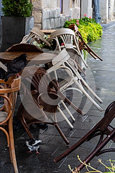 Empty wet wooden table and chairs on terrace of outdoor cafeteria during rain. Street city life in rain