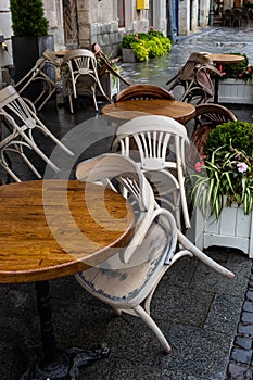 Empty wet wooden table and chairs on terrace of outdoor cafeteria during rain. Street city life in rain