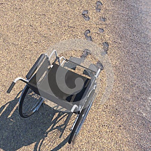 Empty wheelchair on a beach of sand with footprints