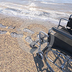 Empty wheelchair on a beach of sand with footprints