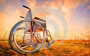 Empty wheelchair on the meadow at sunset