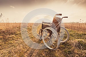 Empty wheelchair on the meadow at sunset - vintage retro version