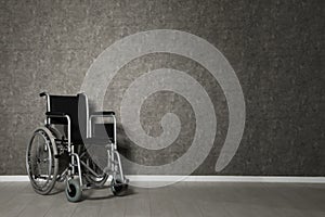Empty wheelchair near grey wall indoors.