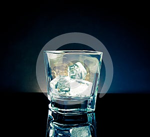 Empty whiskey glass with ice and light tint blue disco on black background