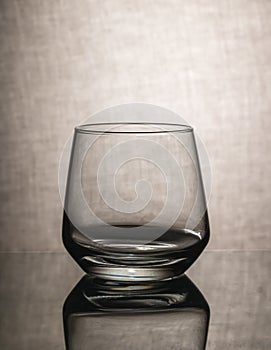 empty whiskey glass with reflection on textured gray background