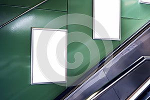 Empty white advertising urban billboard indoor in subway hall, vertical portrait, green walls, above metallic stairs.