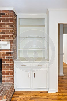 An empty white built in bookcase in a living room next to a red brick fireplace