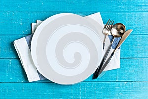Empty white ceramic round plate with table cloth,knife,spoon and fork on blue wooden background