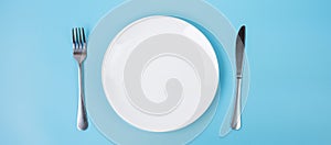 Empty white ceramics plate with knife and fork on blue background. dining and kitchenware concept