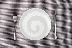 Empty white ceramics plate with knife and fork on table background. dining and kitchenware concept