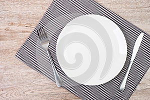 Empty white ceramics plate with knife and fork on table background. dining and kitchenware concept