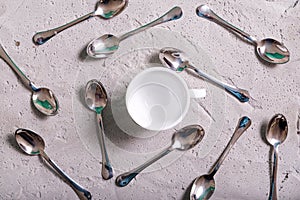 Empty white coffee cup and coffee spoons scattered around the cup on a concrete surface
