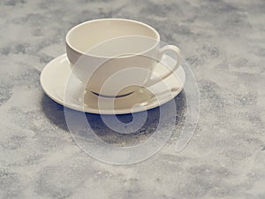 Empty white cup with saucer on a gray concrete background