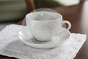 An empty white cup and a saucer stand on a wooden table.