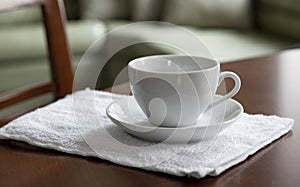 An empty white cup and a saucer stand on a wooden table.