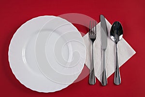 Empty white dinner plate with silver fork and Dessert Tablespoon, isolated on red tablecloth background with copy space. Table Set