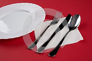 Empty white dinner plate with silver fork and Dessert Tablespoon, isolated on red tablecloth background with copy space. Table Set