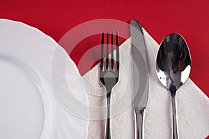 Empty white dinner plate with silver fork and Dessert Tablespoon, isolated on red tablecloth background with copy space. Table Set