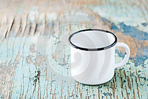 Empty white enameled mug on an old wooden table. Dishes for camping and travel. Copy space