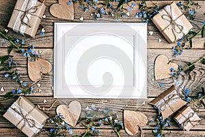 Empty white frame with forget-me-not flowers, gifts and hearts on old wooden boards