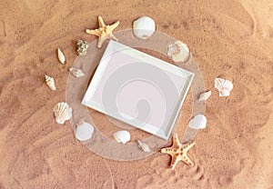 Empty white frame, starfishes and seashells on sand beach. Summer holidays concept