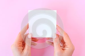 Empty white paper in female hands on a pink background, as mockup for your design.