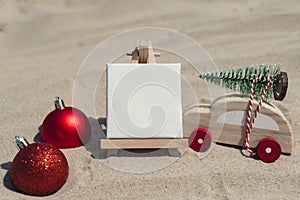 Empty white paper note frame with copy space for your text or design displays on sandy beach. Christmas balls car with