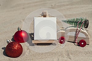 Empty white paper note frame with copy space for your text or design displays on sandy beach. Christmas balls car with