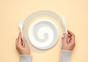 Empty white paper plate and female hands are holding disposable fork and knife