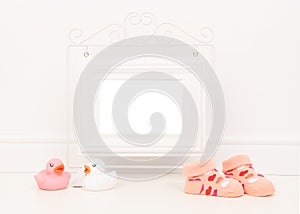 Empty white picture frame with space for text or wishes in a white living room setting with pink baby sock and pink and white rubb